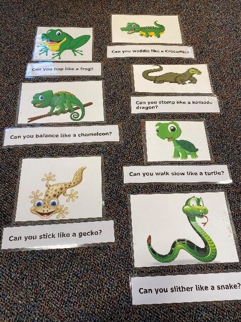 Photo of laminated cards with images of different reptiles, turtles, and amphibians accompanied by action prompts (e.g. Can you slither like a snake?)