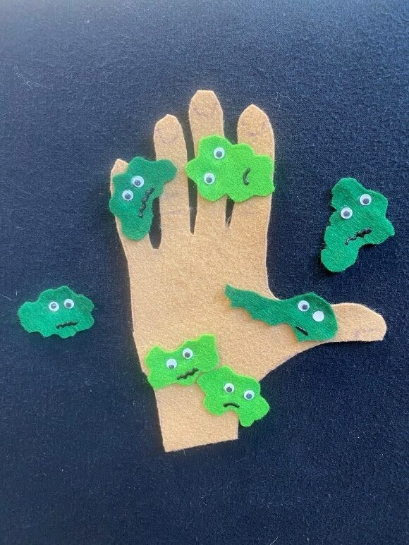 Photo of a hand and globby green "germs" made out of felt and stuck to a flannel board.