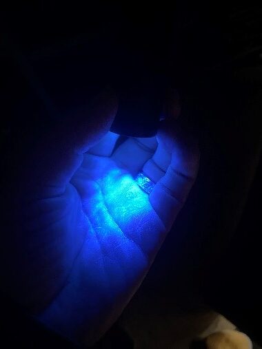 Dark photo of a hand under UV light, with a glowing substance on the palm.