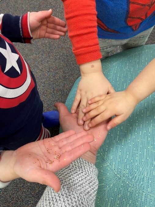 Photo of a stack of hands, one adult and three child, covered with golden glitter.